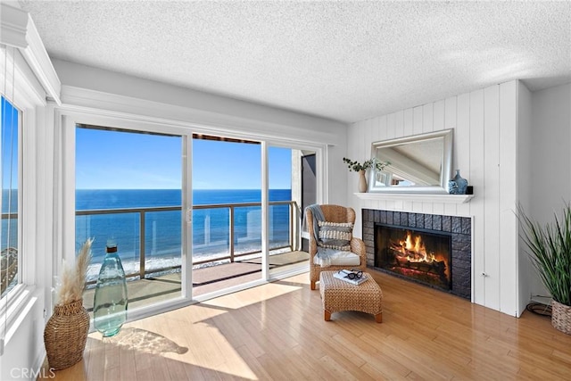 sitting room featuring a textured ceiling, a water view, wood finished floors, and a brick fireplace