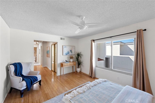 bedroom featuring a ceiling fan, light wood-style flooring, visible vents, and a textured ceiling