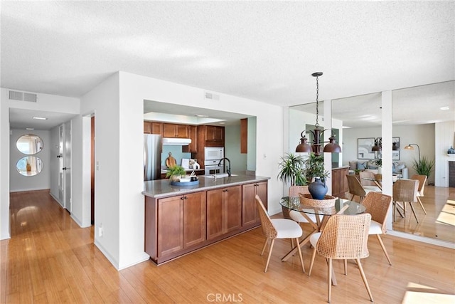 kitchen with brown cabinets, open floor plan, decorative light fixtures, freestanding refrigerator, and under cabinet range hood