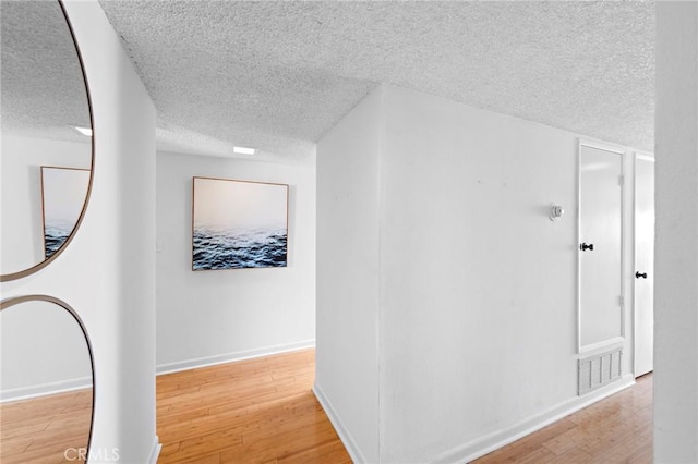 hallway featuring a textured ceiling, wood finished floors, visible vents, and baseboards