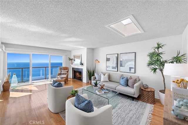 living room featuring a warm lit fireplace, a water view, a textured ceiling, and wood finished floors