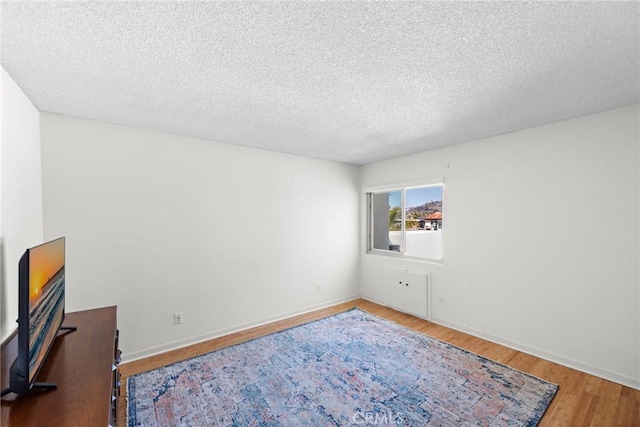 bedroom with a textured ceiling, baseboards, and wood finished floors