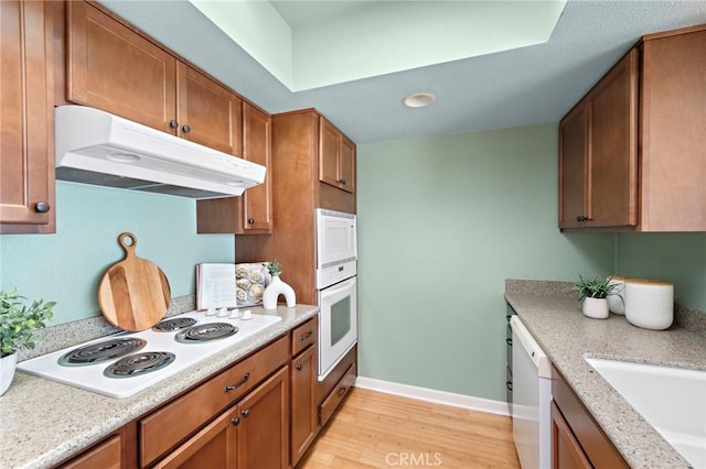 kitchen with light wood-style flooring, white appliances, brown cabinets, and under cabinet range hood