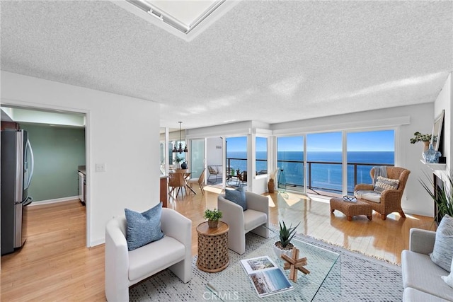 living area featuring a textured ceiling, a water view, light wood-style flooring, and baseboards