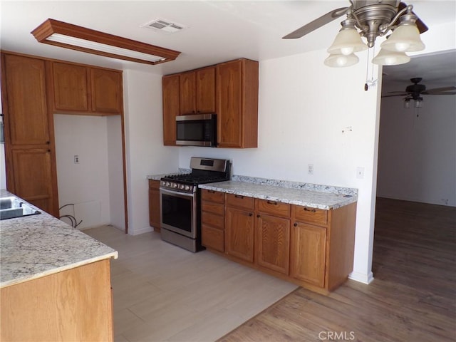 kitchen with appliances with stainless steel finishes, brown cabinetry, visible vents, and a ceiling fan