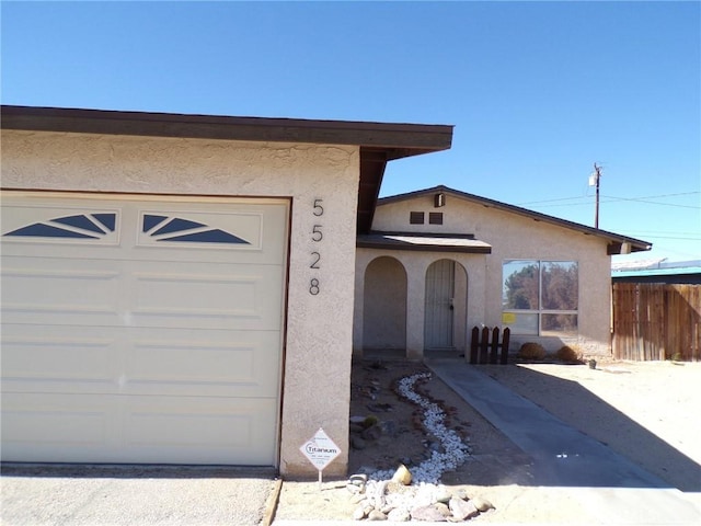 view of front of property featuring an attached garage, fence, and stucco siding