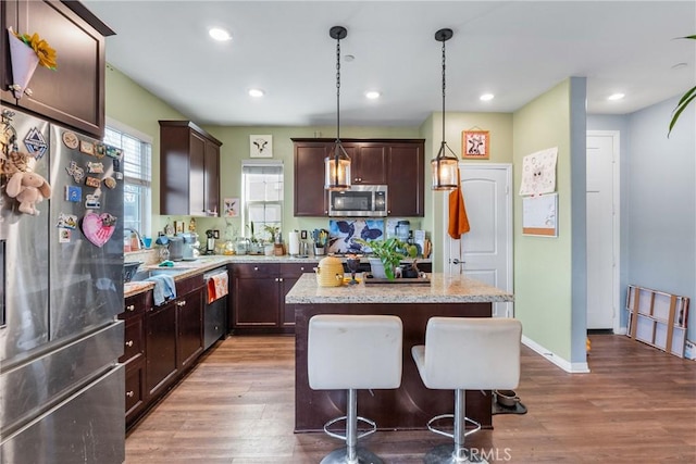 kitchen featuring appliances with stainless steel finishes, wood finished floors, decorative light fixtures, a center island, and a sink