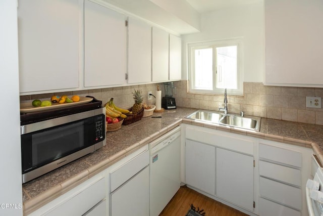 kitchen with stainless steel microwave, backsplash, white cabinetry, a sink, and dishwasher