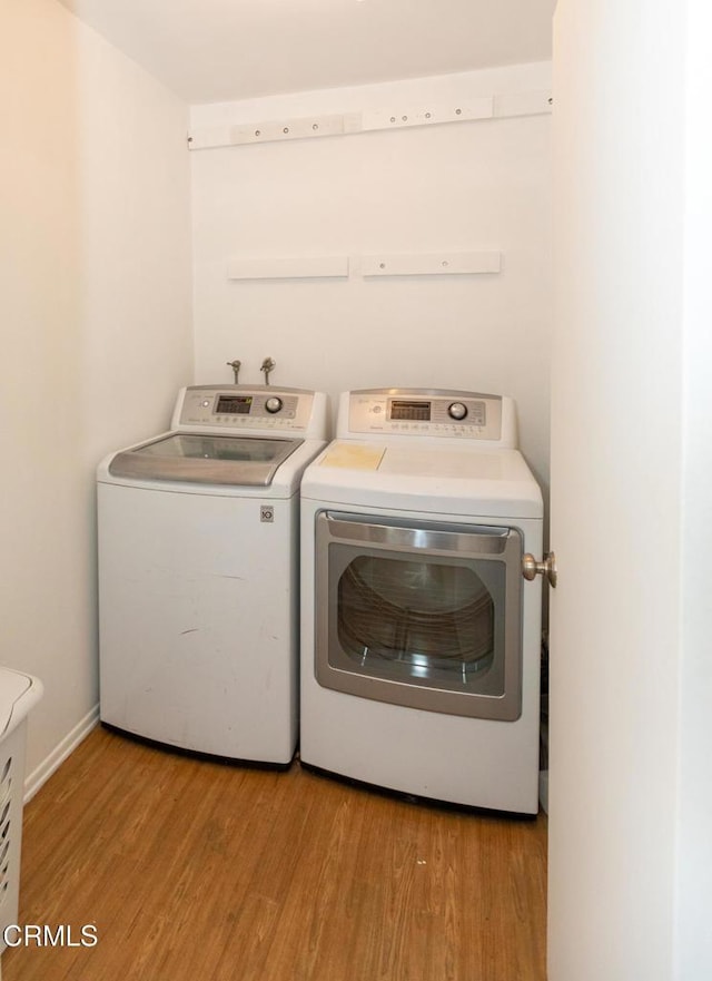 clothes washing area featuring baseboards, laundry area, independent washer and dryer, and light wood-style floors