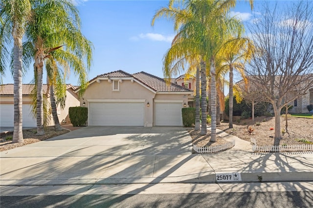 mediterranean / spanish house with driveway, an attached garage, a tiled roof, and stucco siding