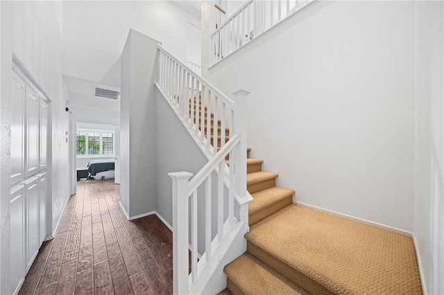 stairs featuring baseboards, visible vents, a high ceiling, and wood finished floors