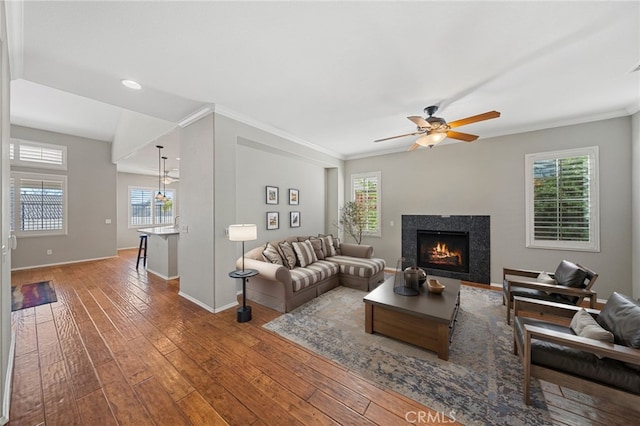 living area featuring crown molding, a high end fireplace, ceiling fan, wood finished floors, and baseboards