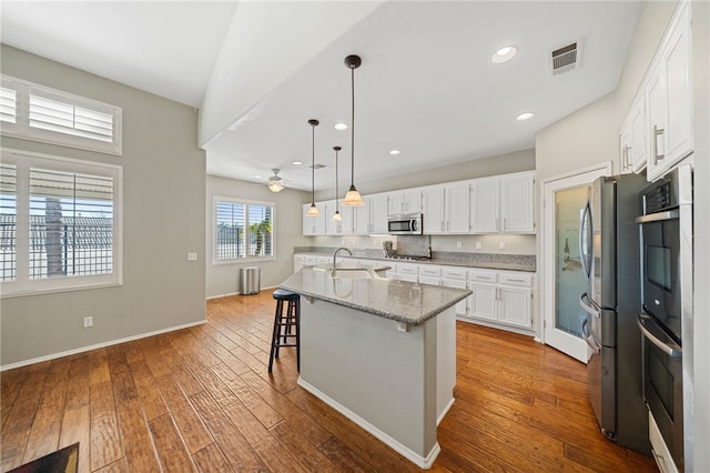 kitchen featuring a kitchen island with sink, stainless steel appliances, visible vents, white cabinetry, and a kitchen breakfast bar