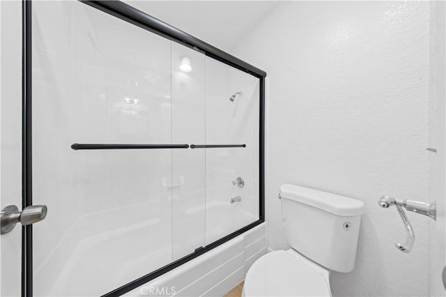 full bathroom featuring enclosed tub / shower combo, a textured wall, and toilet