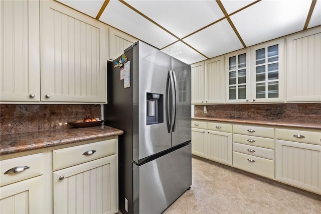 kitchen with glass insert cabinets, dark countertops, stainless steel refrigerator with ice dispenser, and cream cabinets