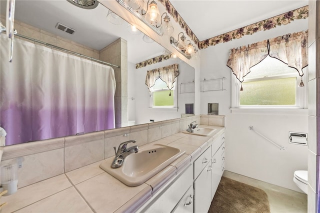 bathroom with toilet, double vanity, a sink, and visible vents