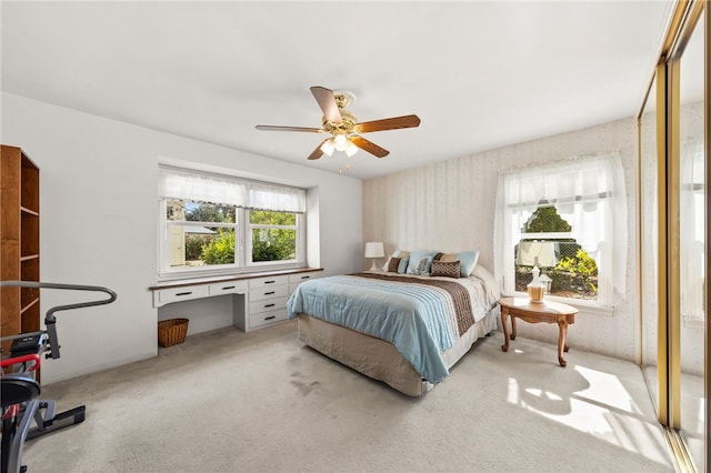 bedroom featuring wallpapered walls, a ceiling fan, built in desk, and light colored carpet