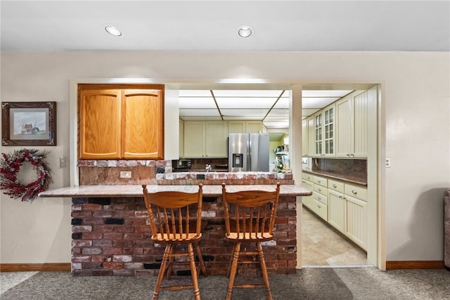 kitchen featuring light colored carpet, a breakfast bar, a peninsula, stainless steel refrigerator with ice dispenser, and green cabinetry