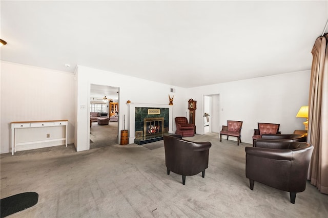 living area with ceiling fan, a tiled fireplace, and light colored carpet