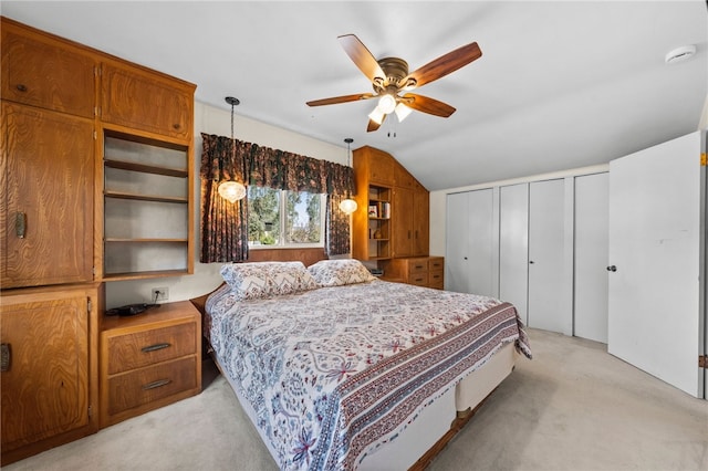 bedroom with vaulted ceiling, ceiling fan, light carpet, and multiple closets