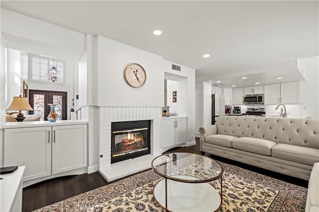 living room with dark wood-style flooring, a brick fireplace, and recessed lighting