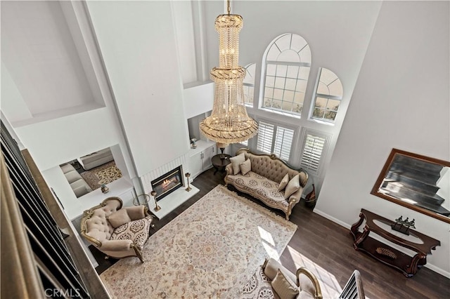 living area with baseboards, dark wood finished floors, a glass covered fireplace, a towering ceiling, and an inviting chandelier