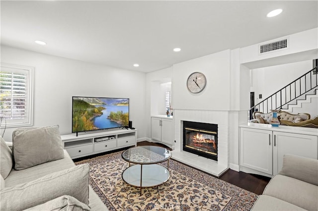 living area with stairway, a glass covered fireplace, visible vents, and recessed lighting