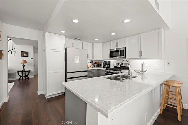 kitchen featuring stainless steel appliances, a peninsula, a sink, and white cabinets