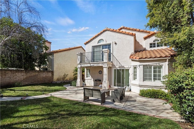 rear view of property with a balcony, a yard, fence, and a patio