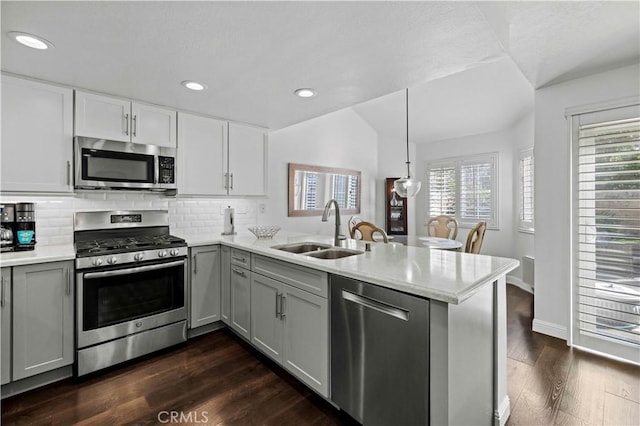 kitchen featuring appliances with stainless steel finishes, a peninsula, light countertops, pendant lighting, and a sink