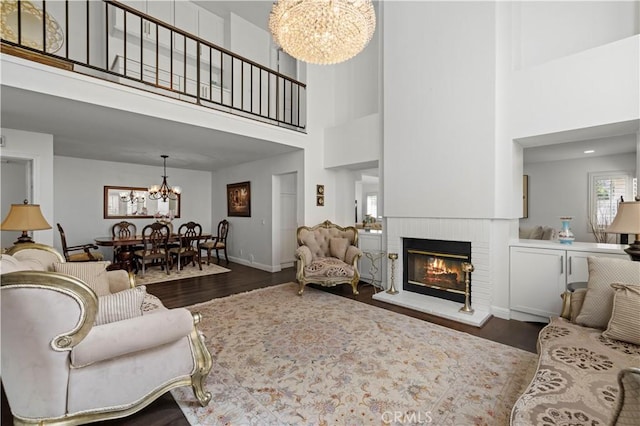 living room featuring a chandelier, a fireplace, baseboards, and wood finished floors