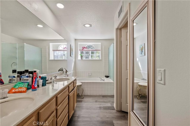 full bathroom featuring double vanity, a sink, a textured ceiling, wood finished floors, and a bath