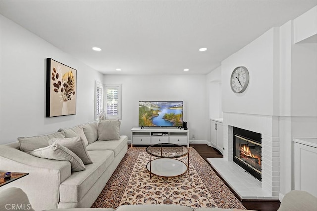 living area with dark wood-style floors, a brick fireplace, baseboards, and recessed lighting