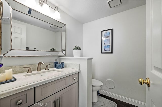 half bathroom with toilet, baseboards, wood finished floors, and vanity