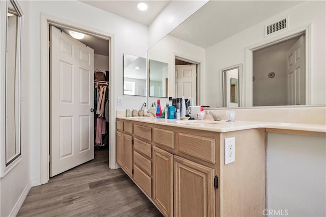 bathroom with double vanity, visible vents, wood finished floors, a walk in closet, and a sink