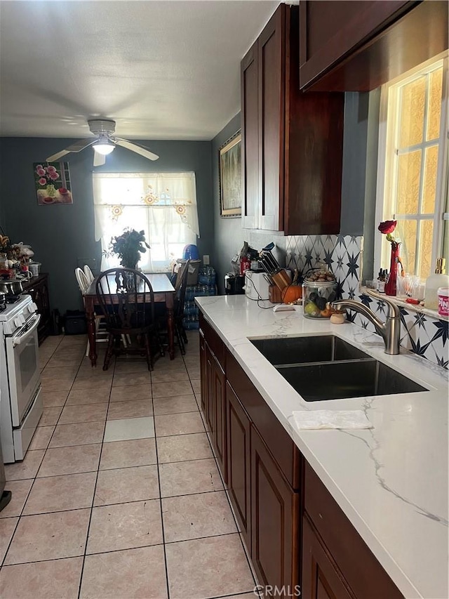 kitchen featuring light tile patterned floors, decorative backsplash, ceiling fan, gas range gas stove, and a sink