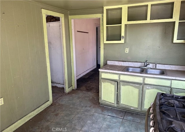 kitchen featuring wood walls, range with gas stovetop, a sink, and light countertops