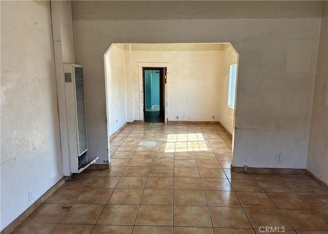 spare room with light tile patterned floors, a heating unit, and baseboards