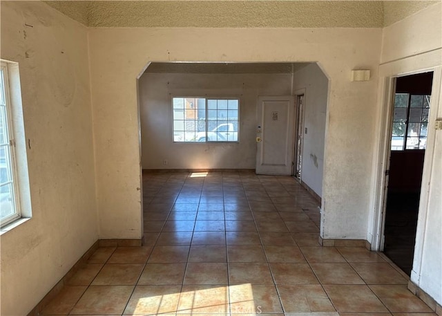 spare room with arched walkways, baseboards, and light tile patterned floors