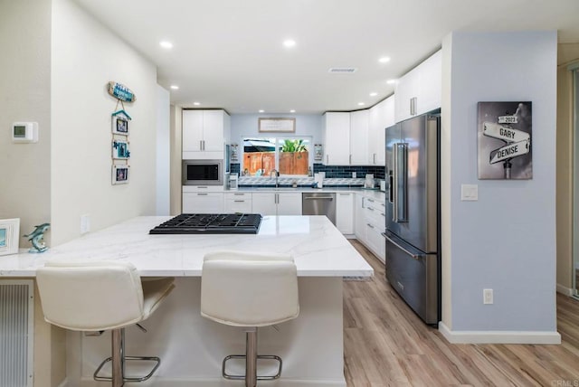 kitchen with light stone counters, a peninsula, appliances with stainless steel finishes, backsplash, and light wood finished floors