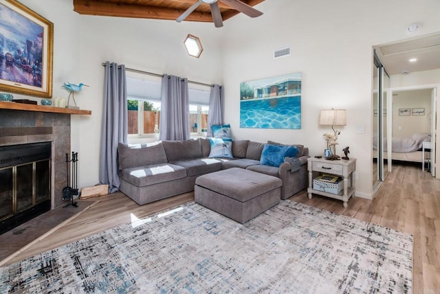 living room featuring visible vents, a tiled fireplace, wood finished floors, high vaulted ceiling, and beam ceiling