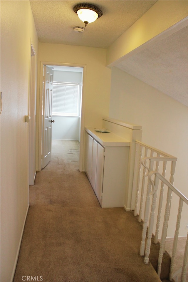 hall with light carpet, a textured ceiling, and an upstairs landing