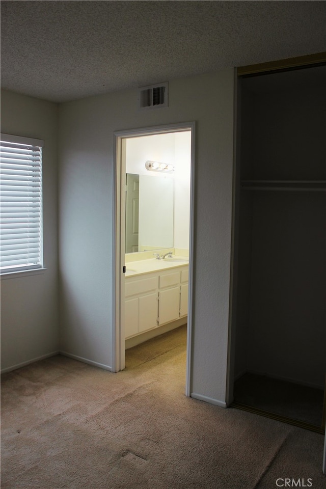 unfurnished bedroom featuring a textured ceiling, baseboards, visible vents, and light colored carpet