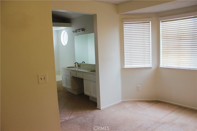 hallway featuring light carpet, a sink, baseboards, and light tile patterned flooring