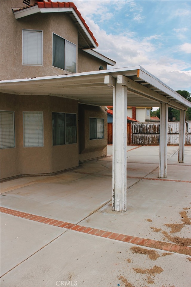 exterior space with a tiled roof, an attached carport, fence, and stucco siding