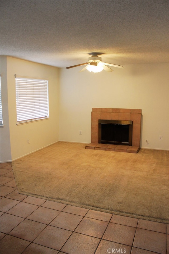 unfurnished living room with carpet floors, ceiling fan, a textured ceiling, and a tiled fireplace