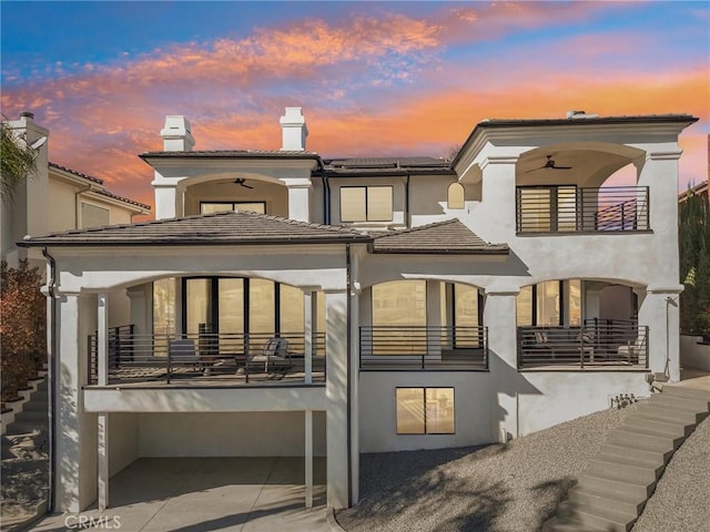 back of property at dusk featuring a balcony, ceiling fan, and stairway