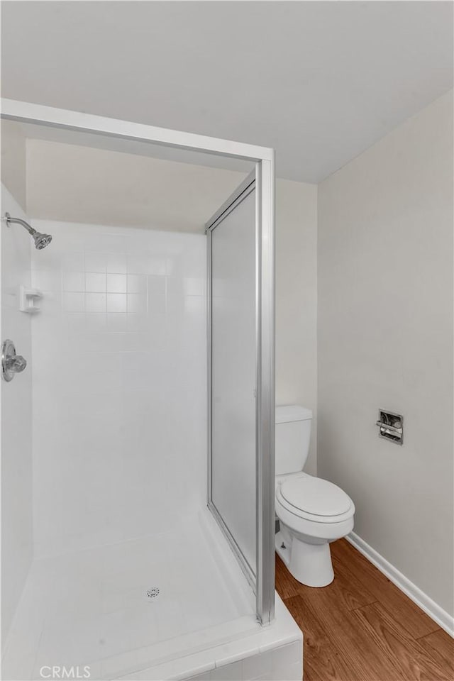 bathroom with toilet, a stall shower, baseboards, and wood finished floors