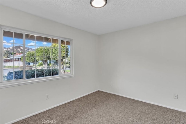 carpeted empty room featuring a textured ceiling and baseboards