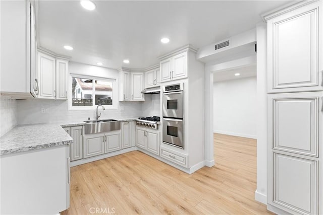 kitchen with appliances with stainless steel finishes, light wood-style flooring, a sink, and visible vents